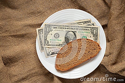 Dollar and a slice of black bread on a white plate on sacking, the price of bread Stock Photo