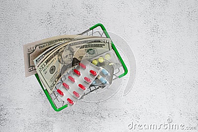 Dollars and pills in a mini grocery basket on a light background. Conceptual image of buying or selling drugs, healthcare, pharmac Stock Photo