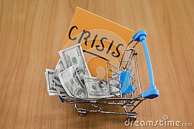 Dollars in a shopping cart and a sticker with the words `crisis`. The concept of economic crisis. Drops in income and solvency. Stock Photo