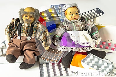 Dolls of elderly couple sit on heap of assorted medicine tablets and pills. Expensive medicines, medical care and treatment for Stock Photo