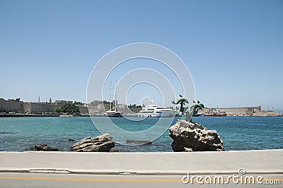 A dolphin statue on the rock in the water by the roadside, opposite of the Rhodes castle Editorial Stock Photo