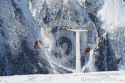 Double-chair ski lift with people on the background of the Caucasus Mountains ridge on a sunny winter day Editorial Stock Photo