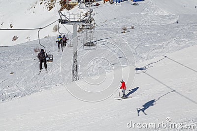 Double-chair ski lift with people over the ski slopes on a sunny winter day Editorial Stock Photo