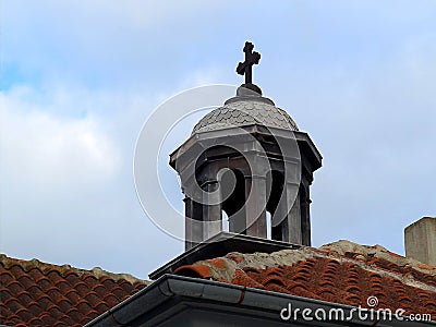 The dome of an old chapel with a cross over the tiled roofs against the sky Stock Photo