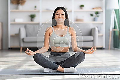 Domestic Yoga. Happy young asian woman meditating at home in lotus position Stock Photo