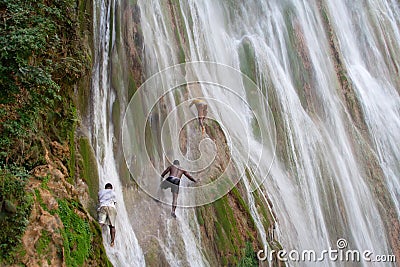 Young guys climb the ledges of a cliff on the waterfall Editorial Stock Photo