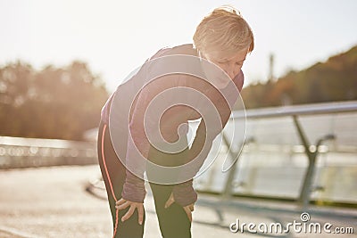 Don`t overdo it. Active mature woman in sportswear looking tired and exhausted, taking a rest after running outdoors on Stock Photo