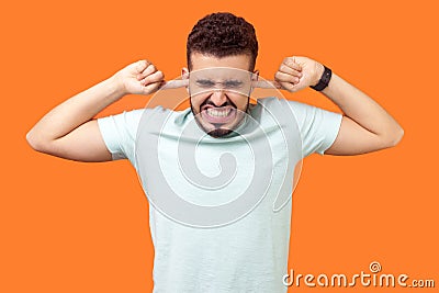 Don`t want to listen anymore. Portrait of brunette man tightly covering his ears. isolated on orange background Stock Photo