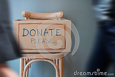 Donation Concept. Empty Donate Box on Chair against Wall in Public Space. blurred walking people as forground Stock Photo