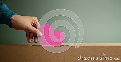 Donation Concept. Hand Dropping a Pink Paper Heart into a Donate Box. Helping, Supporting and Togetherness. Stock Photo