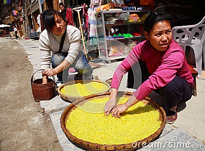 ethnic women treated with rice on a street Zhaoxing Village. Yellow rice is found in large wicker baskets. Zhaoxing Town Editorial Stock Photo