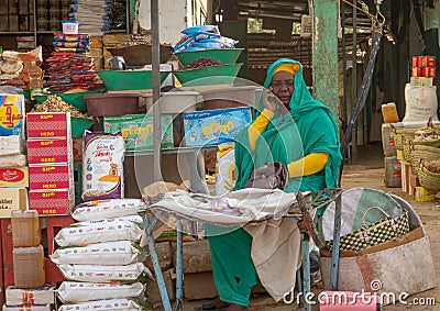 Elderly woman calling her mobile phone in green Abaya at a sales booth in the market of Dongola Editorial Stock Photo