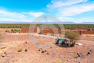 Donkey with cart and adobe houses in the foreground and palm forest and mountains of the Draa Valley, Zagora, Morocco. Bonfire Stock Photo