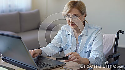 Donna adulta felice nel numero di carta entrante della sedia a rotelle sul computer portatile, comperante online video d archivio Donna adulta felice nel numero di carta entrante della sedia a rotelle sul computer portatile, comperante online video d archivio