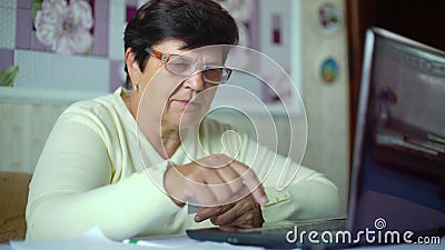 Donna anziana senior in occhiali che controlla i costi delle spese quotidiane sul computer portatile a casa stock footage Donna anziana senior in occhiali che controlla i costi delle spese quotidiane sul computer portatile a casa stock footage