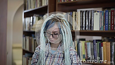 Donna graziosa dei pantaloni a vita bassa in vetri con i dreadlocks che scelgono libro per la lettura sul tempo libero alla bibli video d archivio Donna graziosa dei pantaloni a vita bassa in vetri con i dreadlocks che scelgono libro per la lettura sul tempo libero alla bibli video d archivio