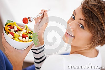 Dont even think about stealing my salad. a young woman looking over her shoulder while eating a salad. Stock Photo