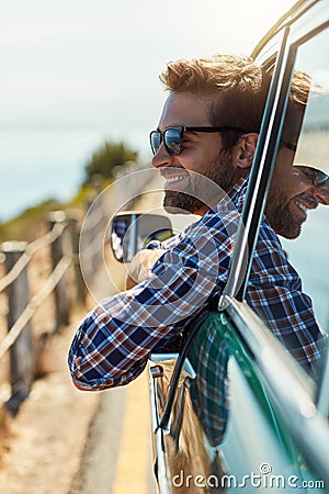 Dont forget to enjoy the journey. a handsome man hanging out of a car window while enjoying a roadtrip. Stock Photo