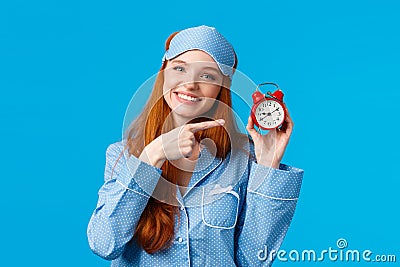 Dont forget wake up on time. Cheerful and cute relaxed feminine redhead woman in pyjama and sleep mask, holding red Stock Photo