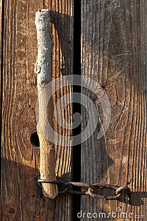 The door to the old barn is closed on a chain. A wooden stick is inserted into the loop Stock Photo