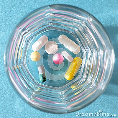 Dose of colorful pills in a transparent glass Cup on a blue background Stock Photo