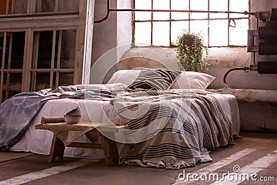 Bed with pillows and blanket, wooden stool and plant in a wabi sabi bedroom Stock Photo