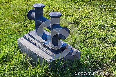 Double cast iron mooring bollard against a background of green grass lawn. Stock Photo