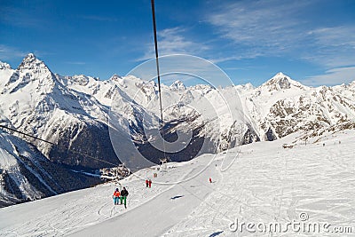 Double-chair ski lift with people over the ski slopes on the background of the Caucasus Mountains ridge on a sunny winter day Editorial Stock Photo