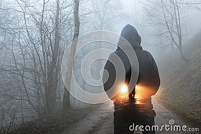 A double exposure concept. A hooded figure looking at a silhouette of a man in front of car headlights. On a spooky forest track o Stock Photo