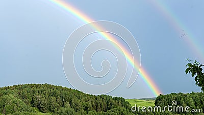 Double rainbow on a gray sky after rain. A rare atmospheric phenomenon after a storm. Beautiful hilly landscape with a real Stock Photo