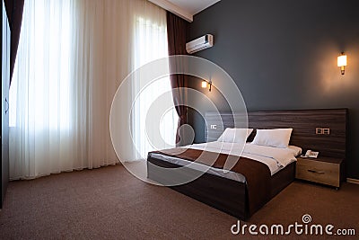 Double wooden bed, with white pillows, bedside tables on the sides, against the blue wall with lamps. Stock Photo