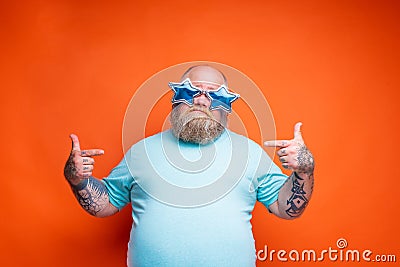 Fat doubter man with beard, tattoos and sunglasses is uncertain for something Stock Photo