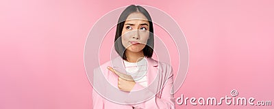 Doubtful business woman, sulking and grimacing while pointing, looking left at banner with skeptical face expression Stock Photo