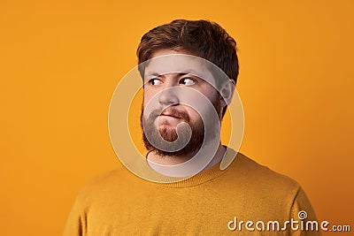 Doubtful hesitant male with ginger hair and beard, closes one eye and looks with clueless expression, makes difficult Stock Photo