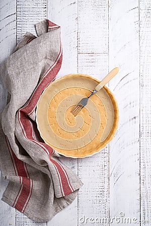 Dough for baking quiche, tart or pie in ceramic baking form ready for bake on kitchen towel over white old rustic plank wooden Stock Photo