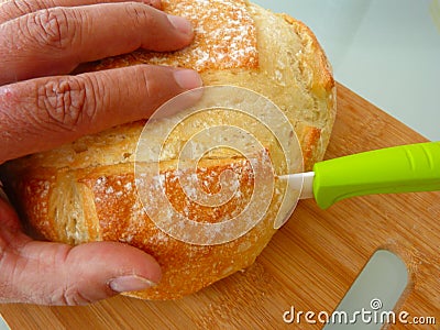 Dough bread slicing close-up view with make hand and green handle ceramic knife Stock Photo