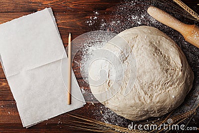 Dough with flour, baking paper, rolling pin, wheat ears on rustic table top view. Homemade pastry for bread or pizza. Stock Photo