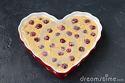 Dough for oatmeal pie with cherries in ceramic form in the shape of a heart on a dark background, Top view Stock Photo