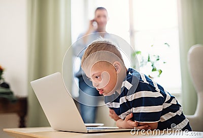 Down syndrome boy with unrecognizable father indoors at home, using laptop. Stock Photo