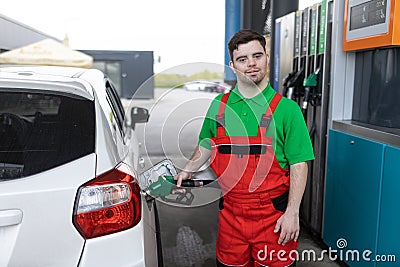 Down syndrome man employee fueling car at gas station. Stock Photo