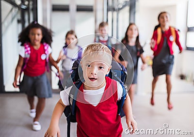 A down-syndrome school boy with group of children in corridor, running. Stock Photo