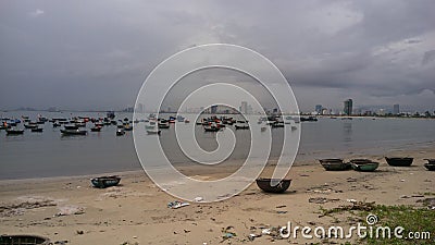 Dozens of fishing boats on a shore of da nang, vietnam. Grey sky, city in the background. Stock Photo