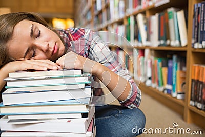 Dozing student sitting on library floor leaning on pile of books Stock Photo