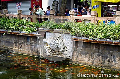 A dragon head carved from stone is used to spray water, and a large number of koi fish gather under the water Editorial Stock Photo
