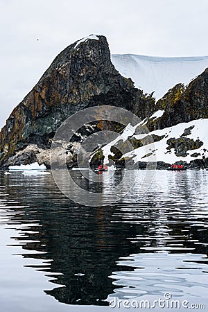 Dramatic Antarctic snow covered and rocky shoreline in Paradise Harbor, Antarctica, with small inflatable rafts cruising in foregr Stock Photo