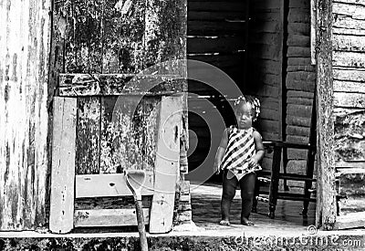 Dramatic black and white image of small Haitian child standing in her doorway of their home looking for her mother. Editorial Stock Photo