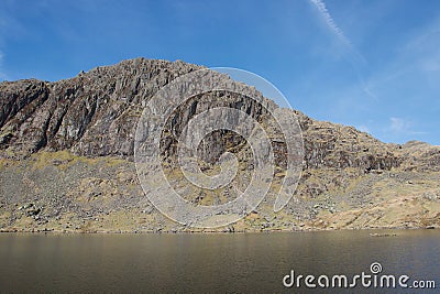 Dramatic cliff and rocky crag above a mountain lake tarn Stock Photo