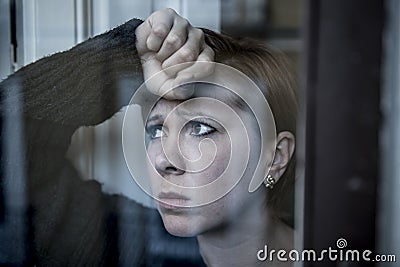 Dramatic close up portrait of young beautiful woman thinking and feeling sad suffering depression at home window looking depresse Stock Photo