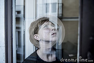 Dramatic close up portrait of young beautiful woman thinking and feeling sad suffering depression at home window looking depresse Stock Photo