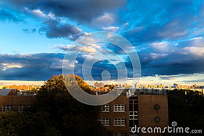 Dramatic clouds moving across a blue sky, while the setting sun adds a golden glow to the urban setting, Bronx, NY, USA Stock Photo